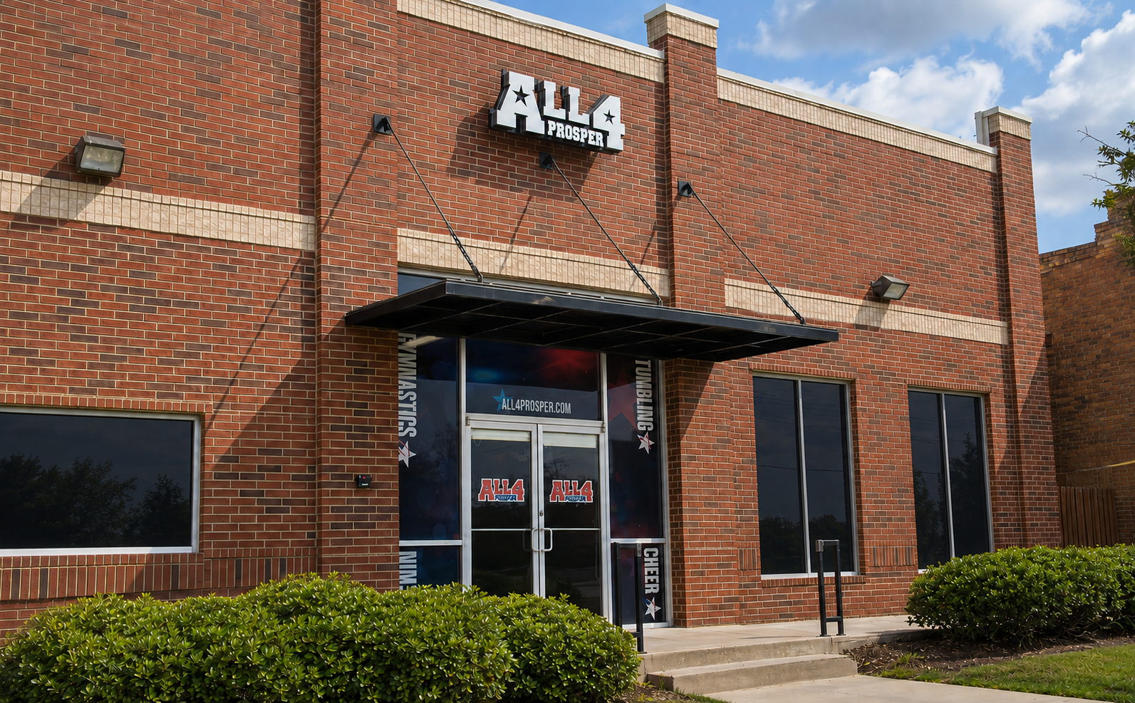 The All 4 Prosper entrance, a red brick building with a black awning over glass doors and the All 4 Prosper sign above.