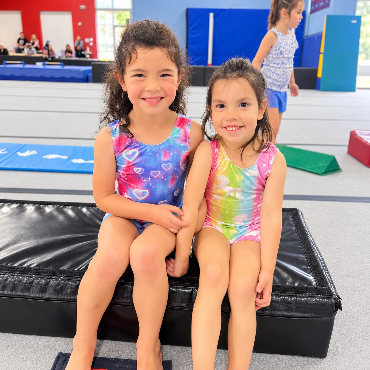 Two smiling young gymnasts sitting together on a mat at All 4 Prosper.